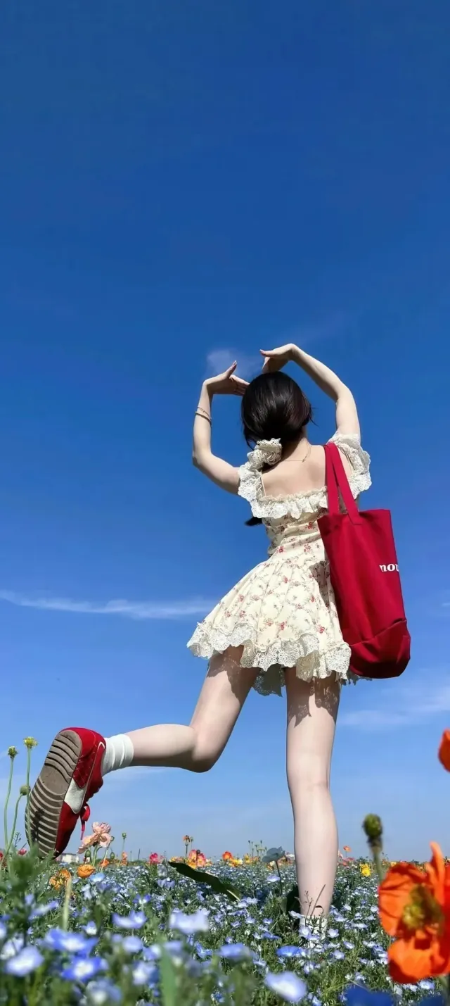 花海中少女跃起比心姿态清新碎花裙红帆布包手机壁纸